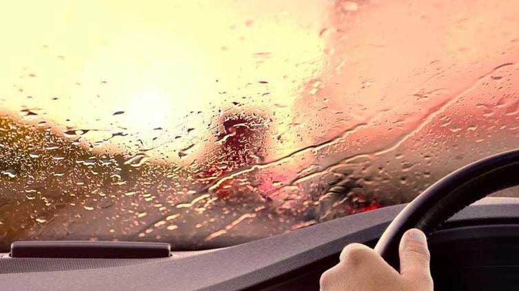 Blurred road scene shown through rain-covered windshield.